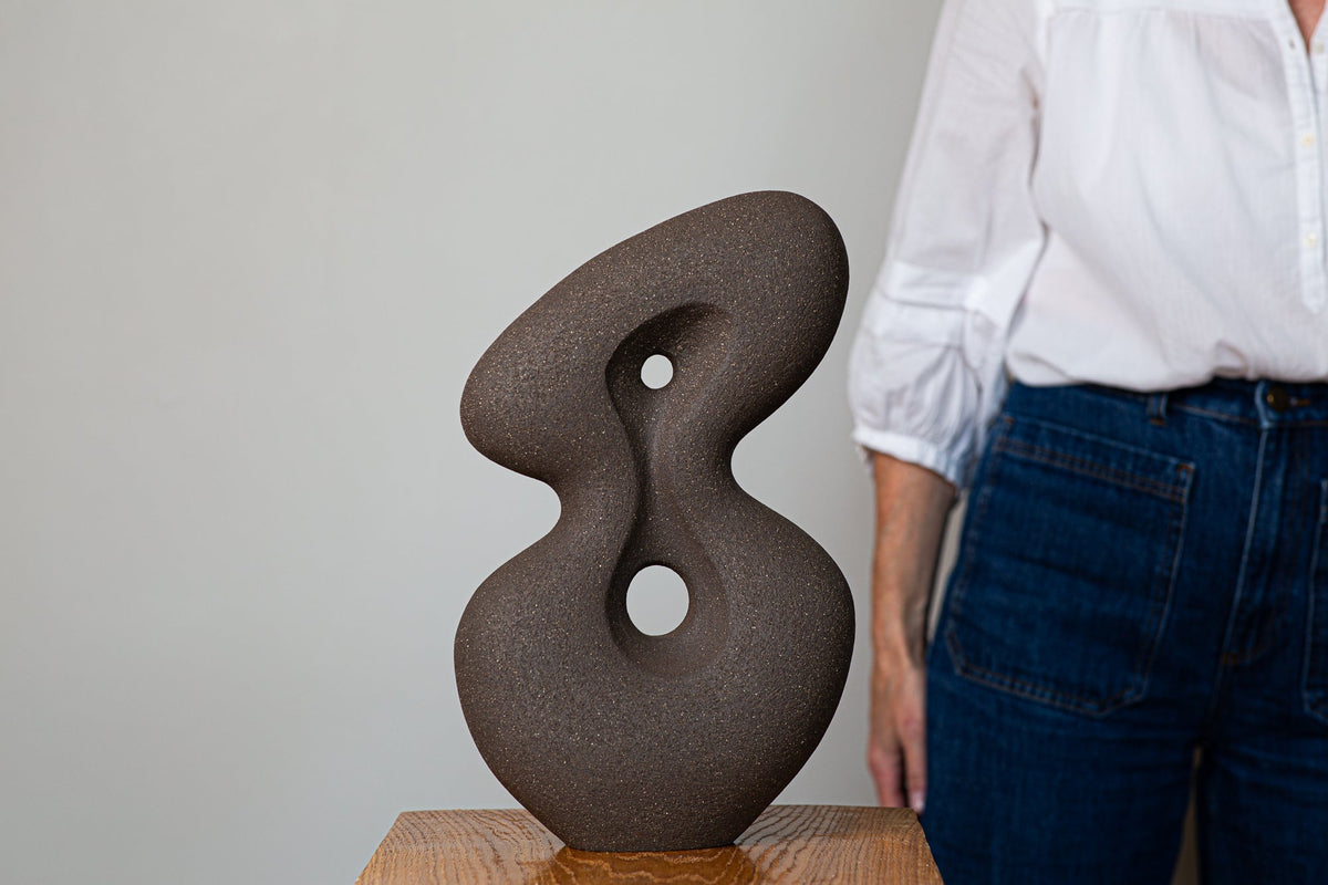 Large hand-built abstract ceramic sculpture by Rachel Peters, in unglazed dark stoneware with two circular negative spaces, shown alongside the artist for scale.