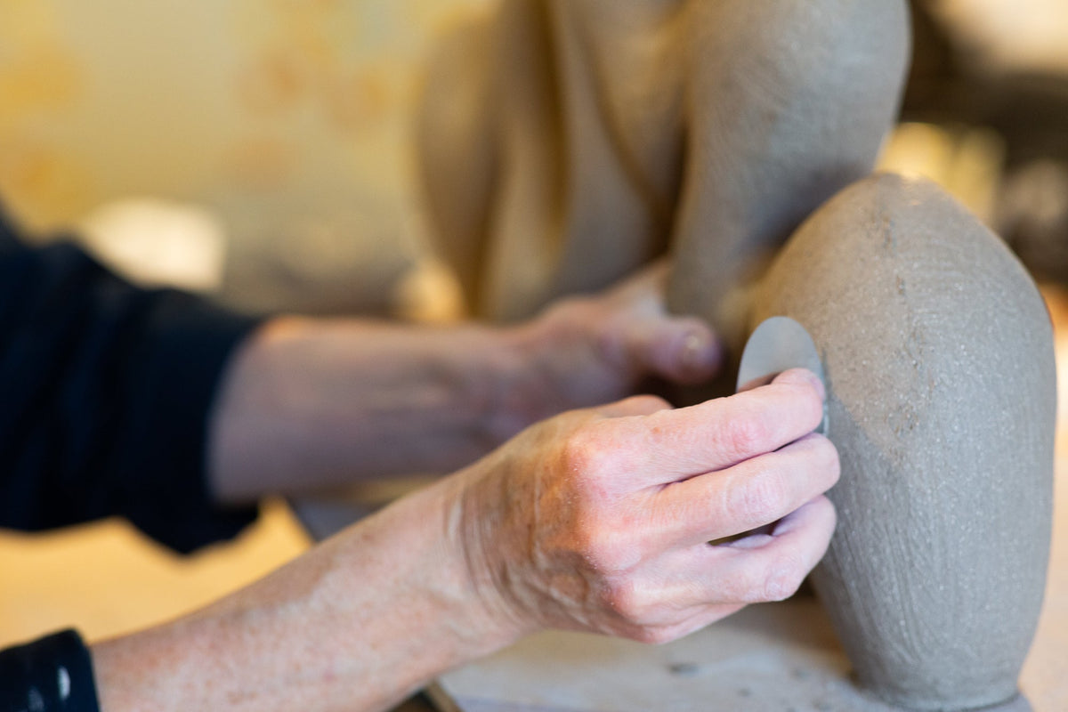Rachel Peters hand-building a ceramic sculpture in her studio, smoothing the surface of an unglazed stoneware form.