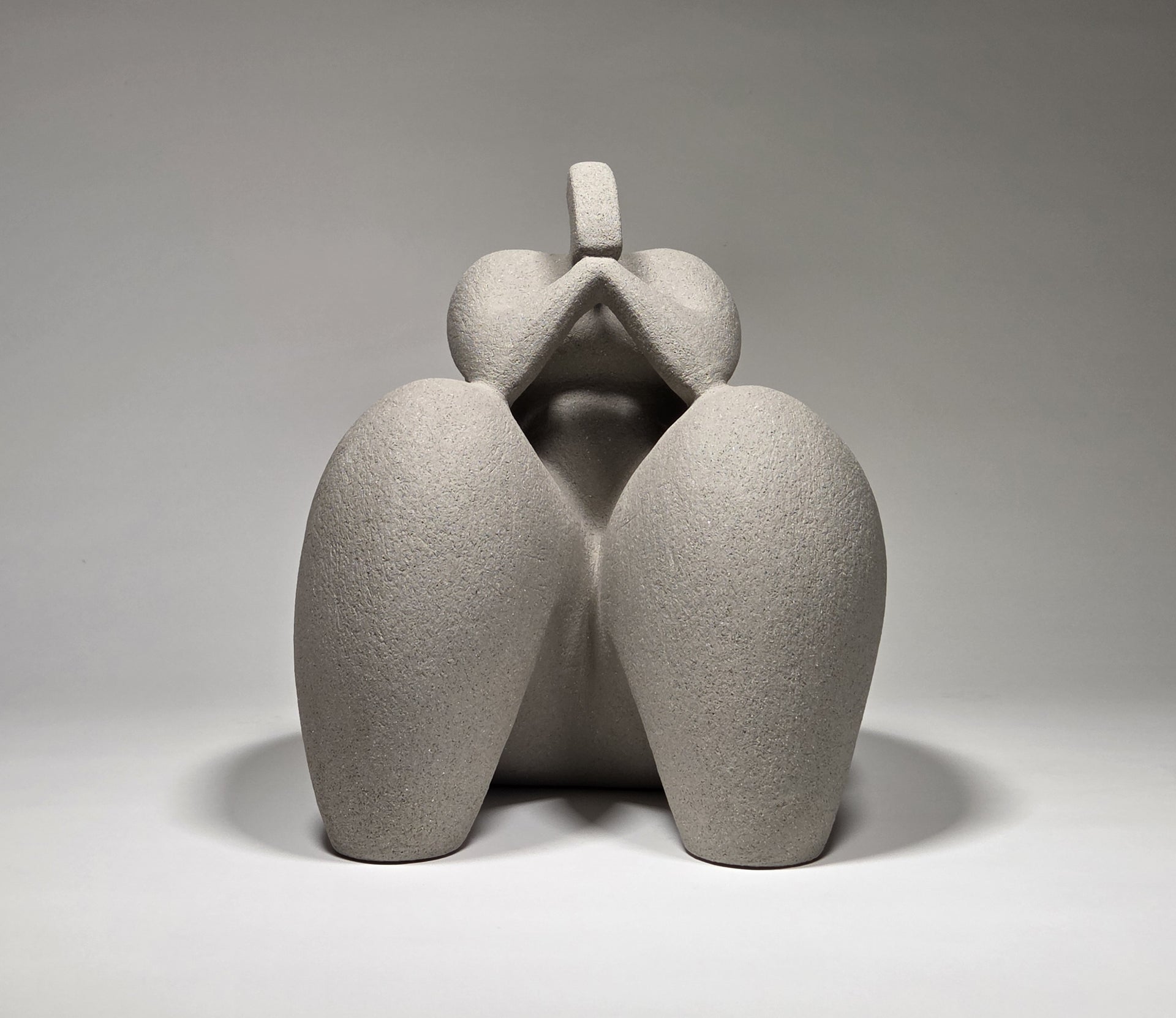 Abstract grey ceramic sculpture of a figure on a grey background