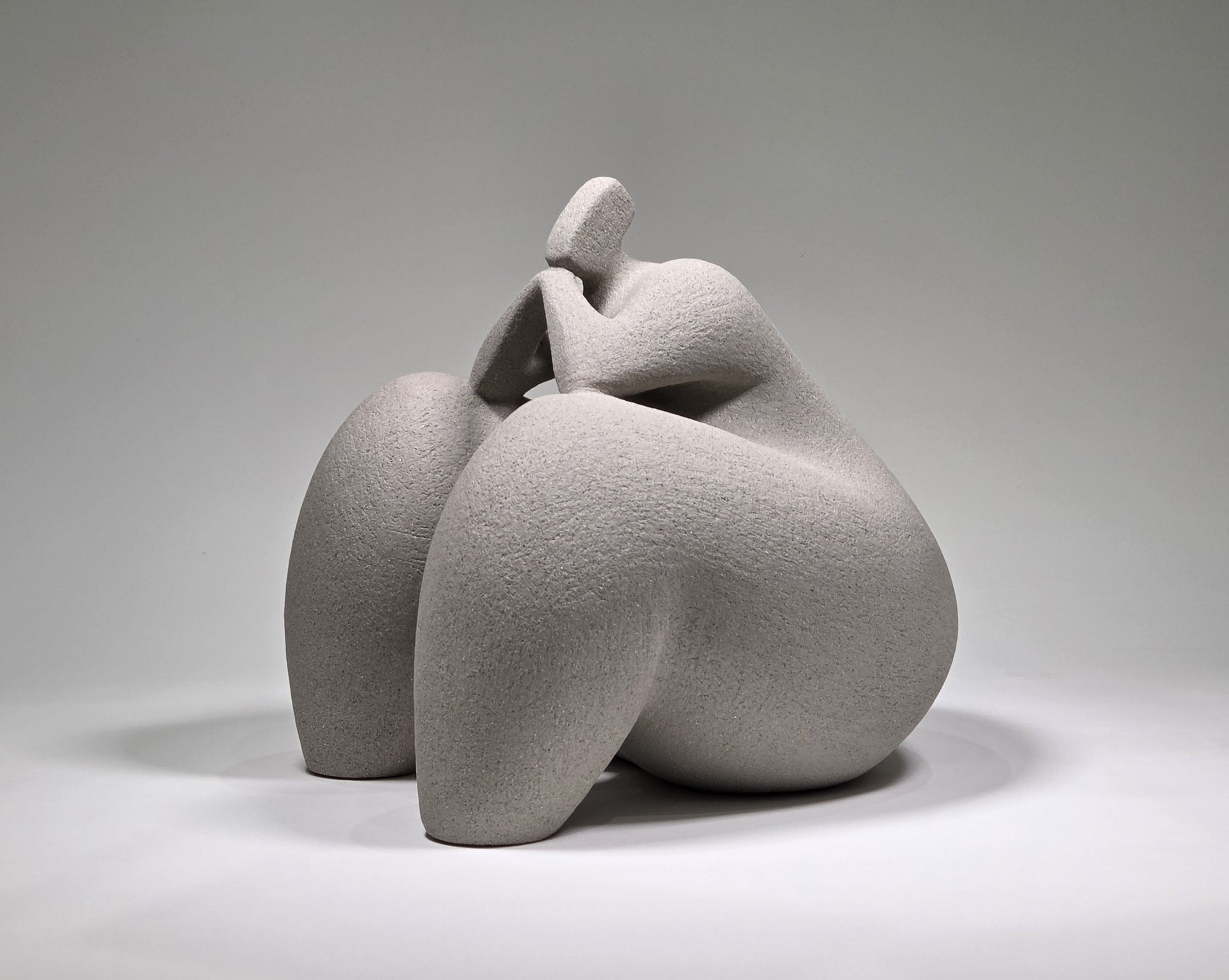 Abstract grey ceramic sculpture of a figure on a grey background