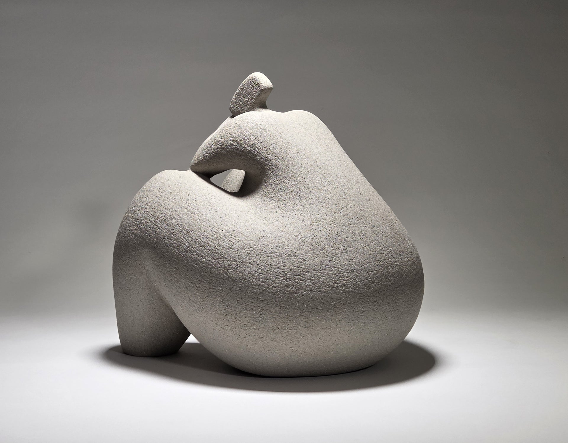 Abstract grey ceramic sculpture of a figure on a grey background