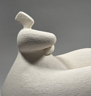 White ceramic sculpture of a reclining figure on a grey background