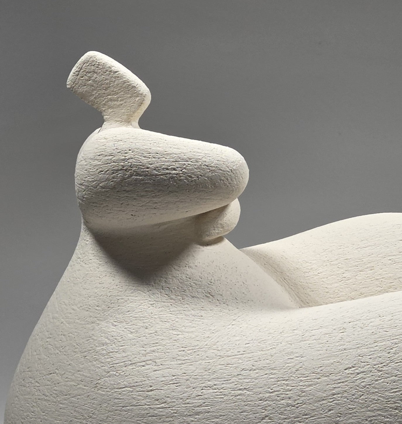 White ceramic sculpture of a reclining figure on a grey background