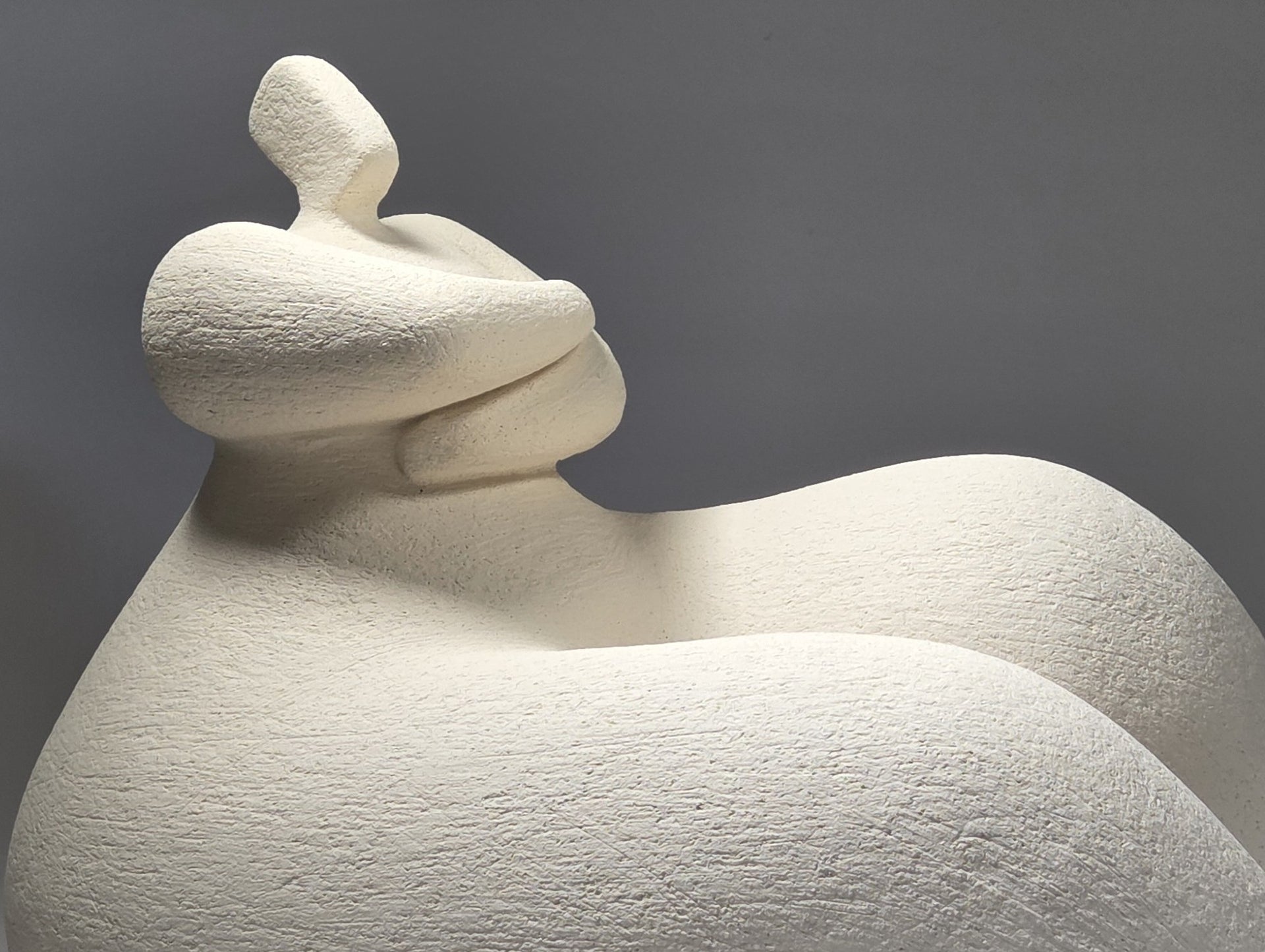 White ceramic sculpture of a reclining figure on a grey background
