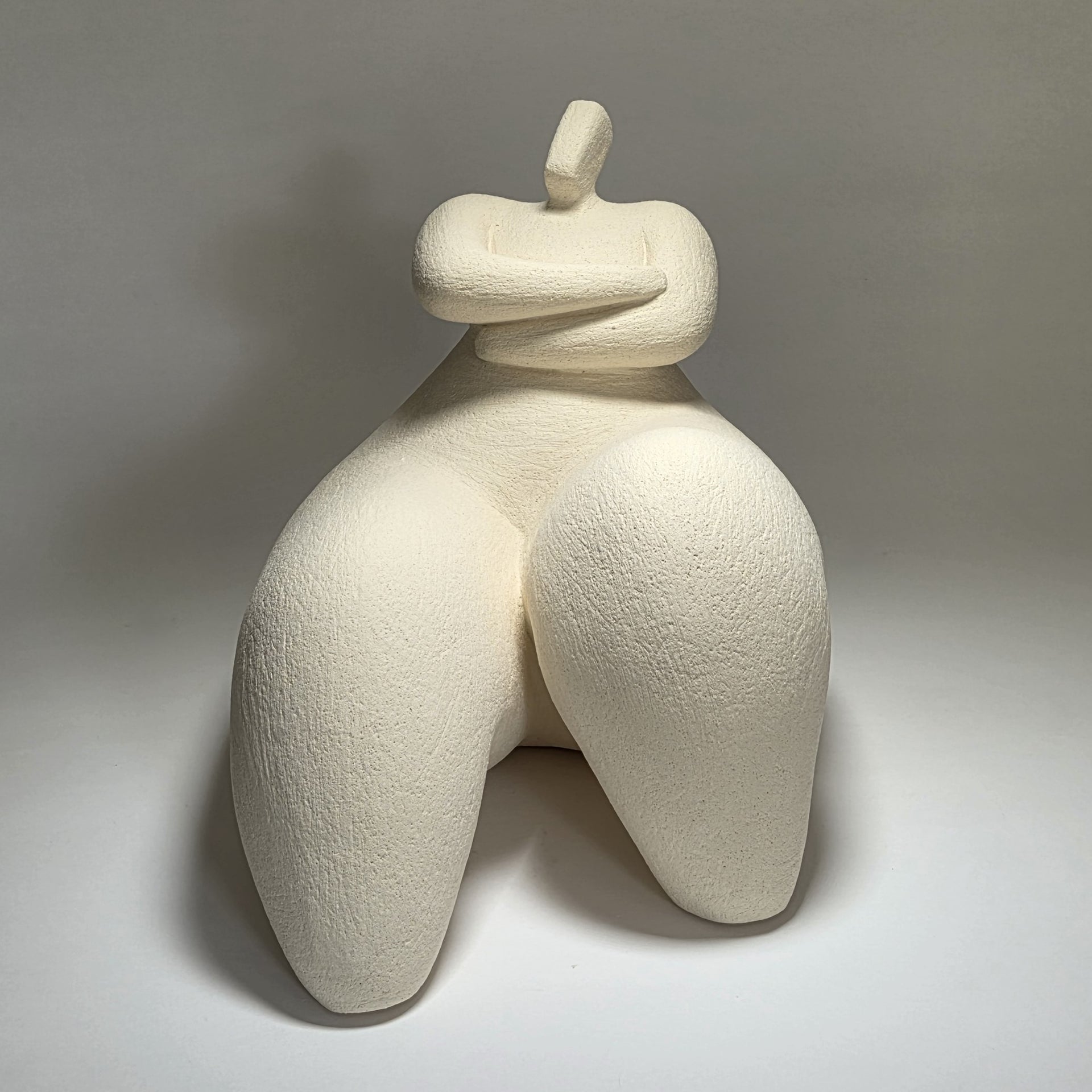 White ceramic sculpture of a reclining figure on a grey background