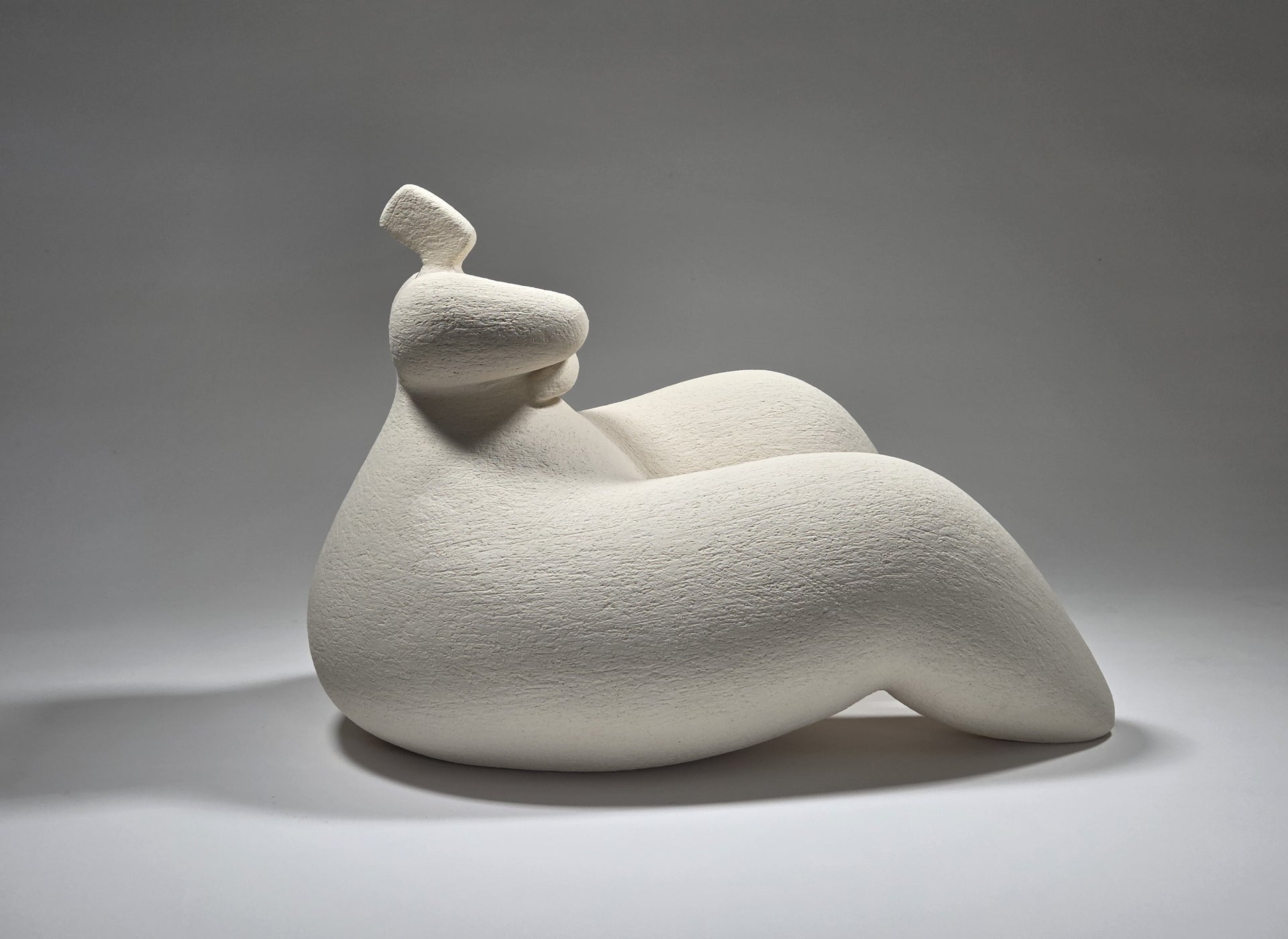 White ceramic sculpture of a reclining figure on a grey background