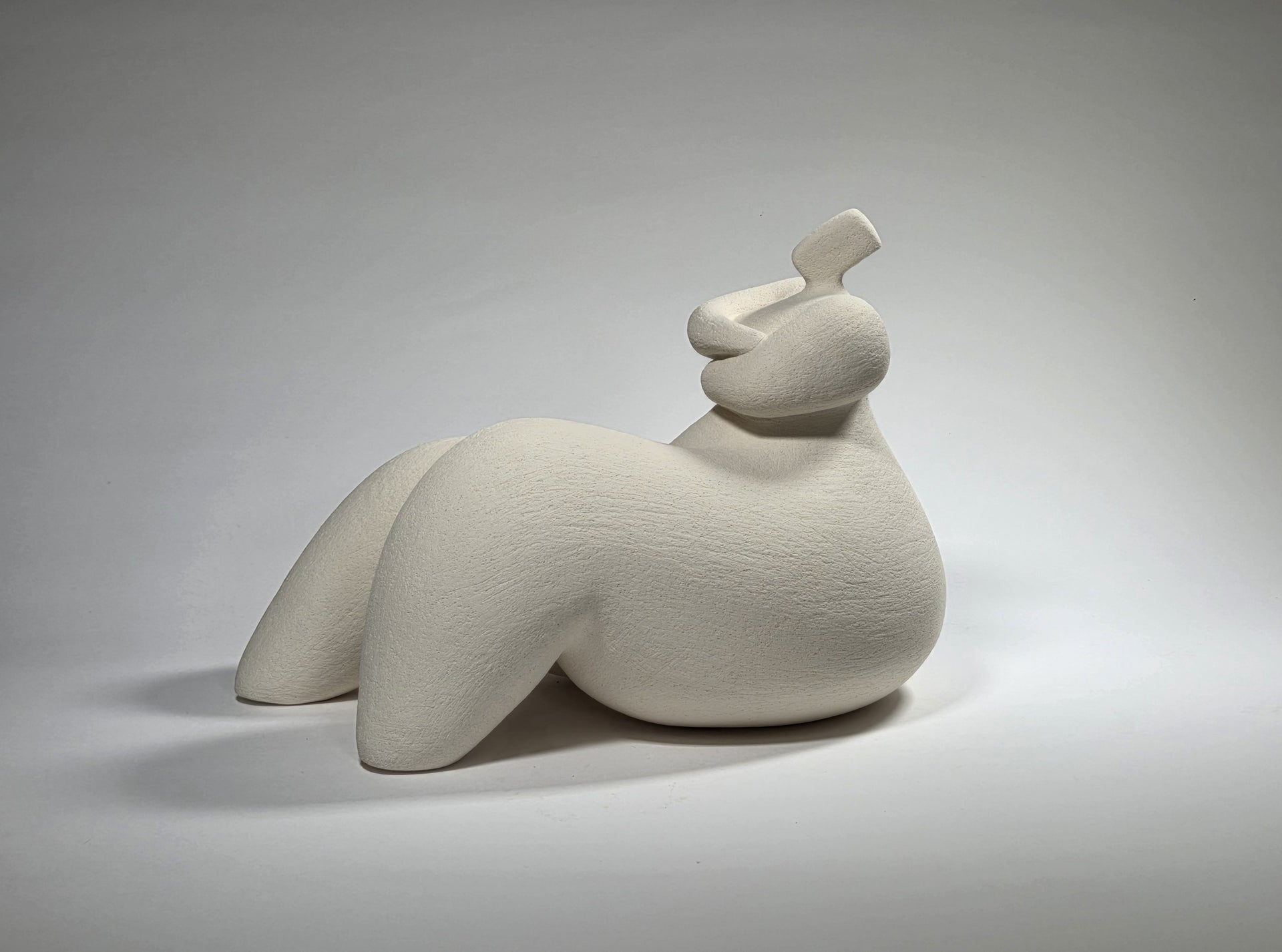 White ceramic sculpture of a reclining figure on a gray background