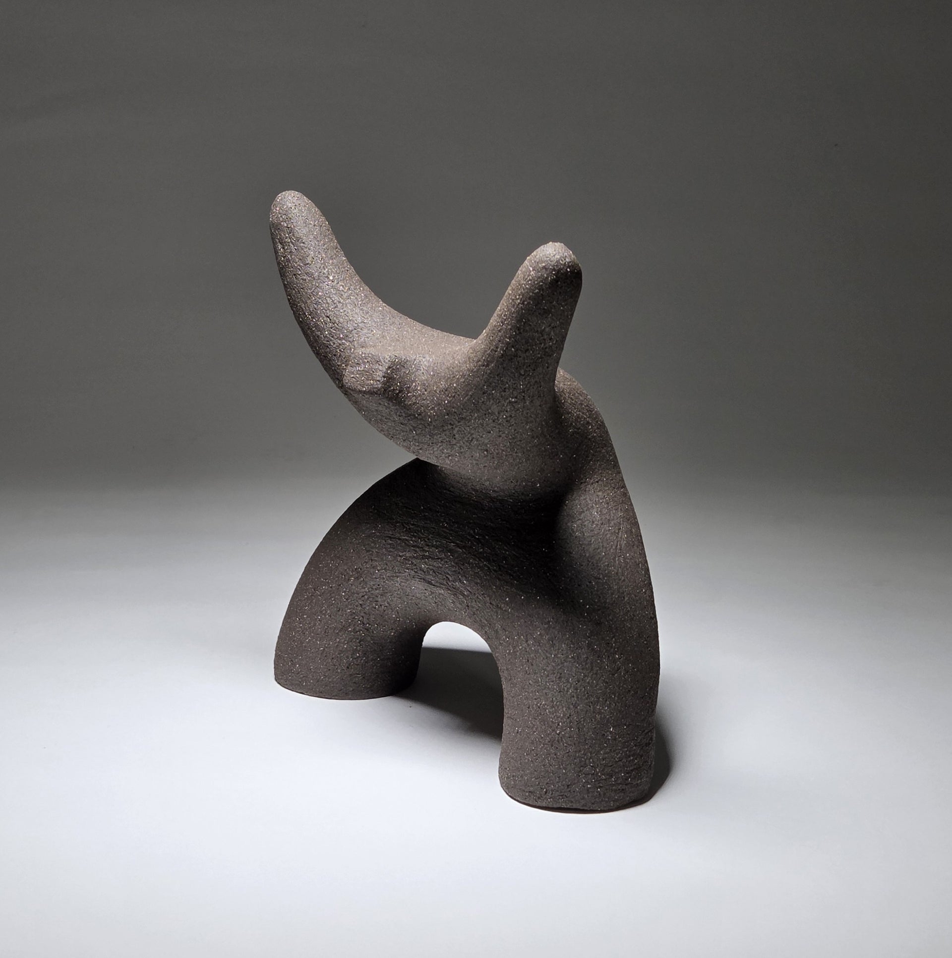 Black abstract ceramic sculpture of a figure bent backwards with arms thrown outwards titled rock star on a light grey background
