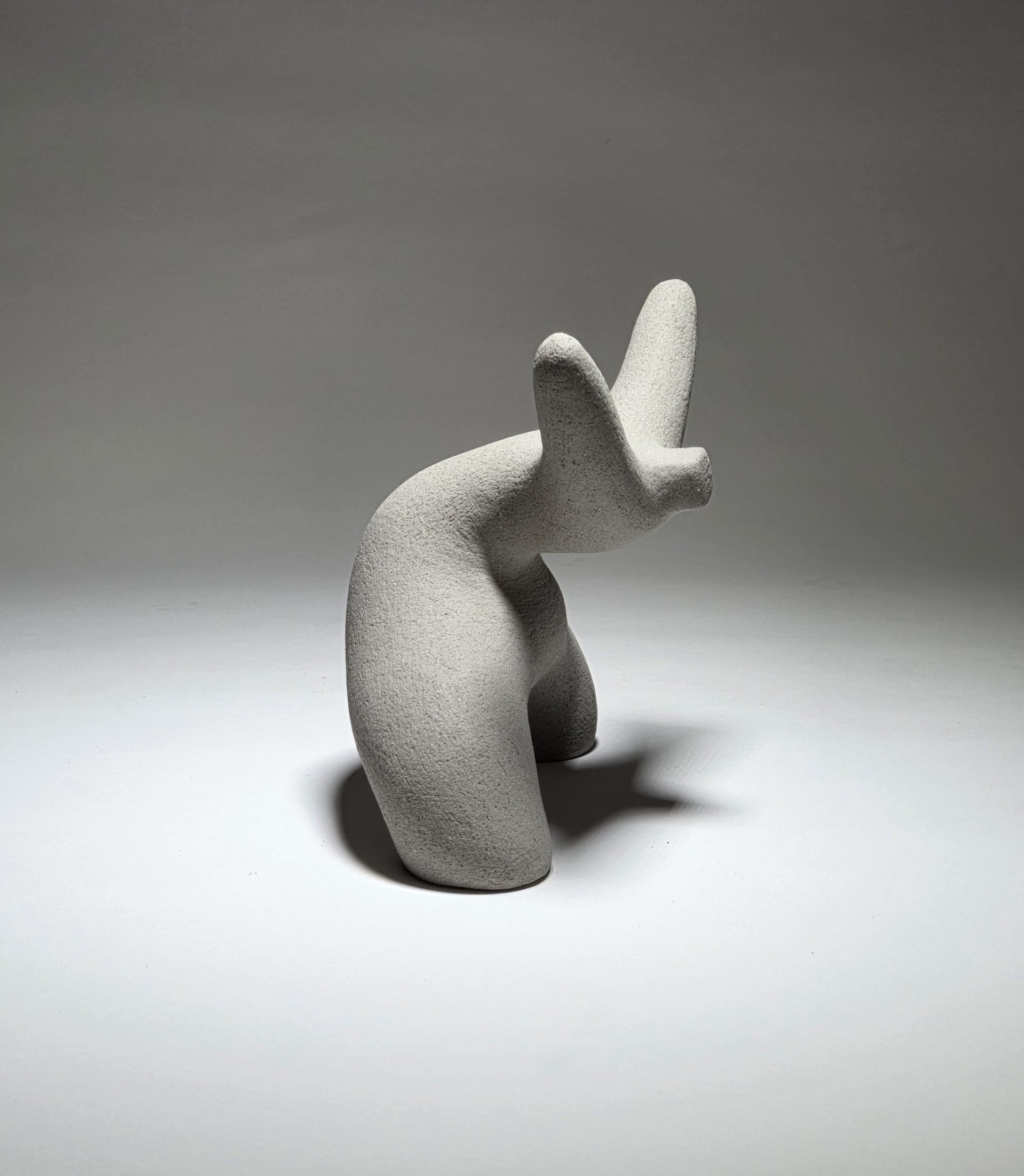 Grey abstract ceramic sculpture of a figure bent backwards with arms thrown outwards titled rock star on a light grey background