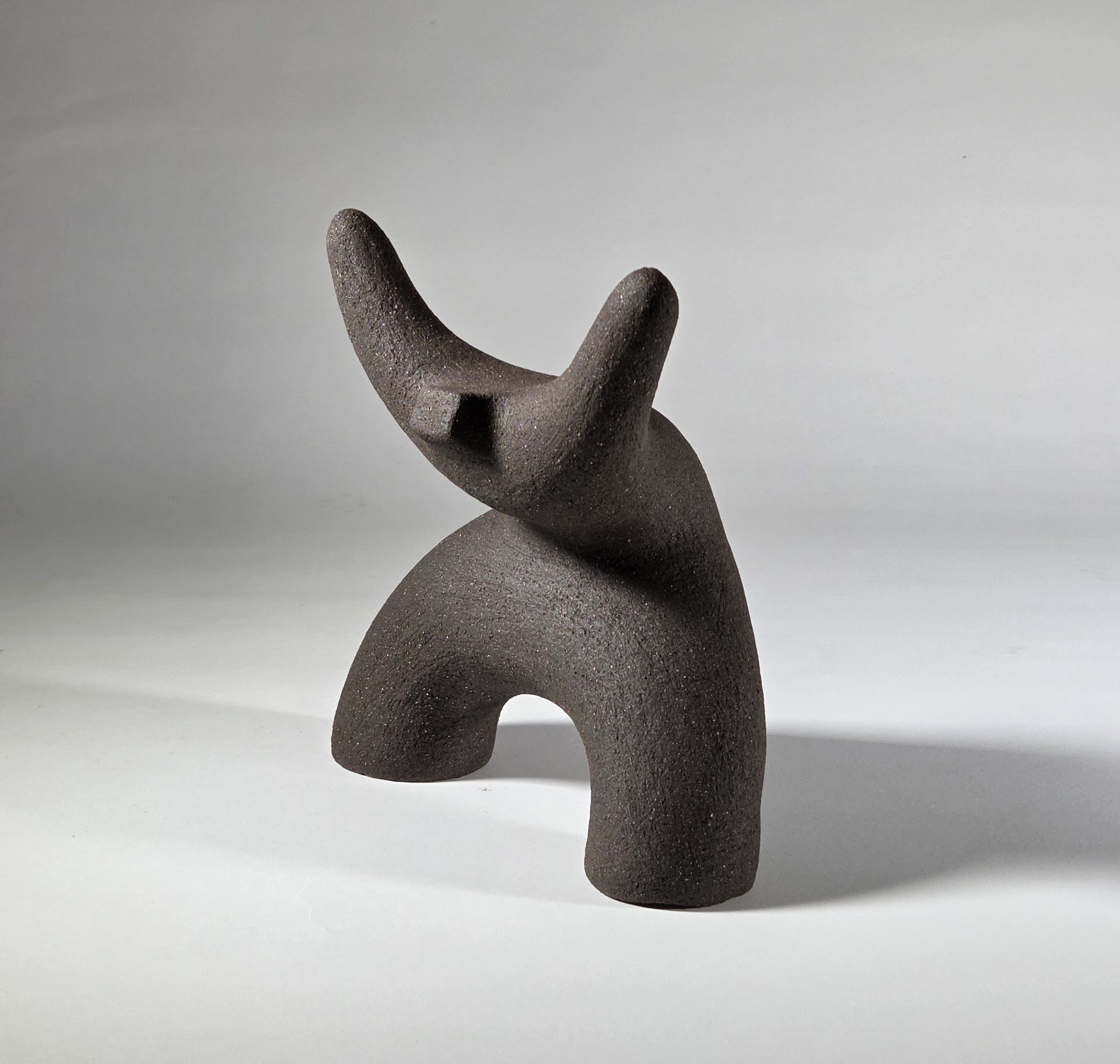 Black abstract ceramic sculpture of a figure bent backwards with arms thrown outwards titled rock star on a light grey background