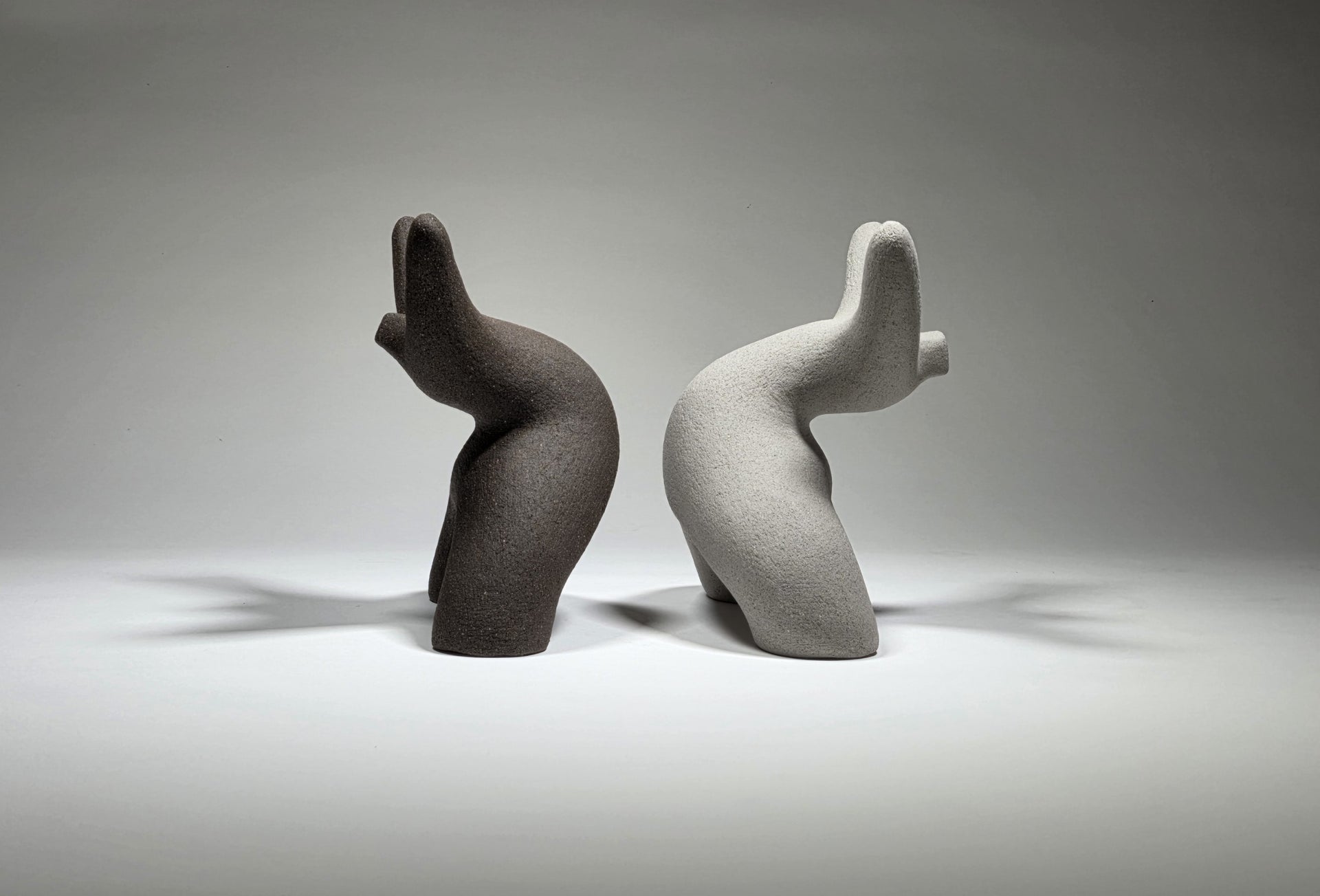 Black and grey abstract ceramic sculptures of two figures bent backwards with arms thrown outwards titled rock star on a light grey background