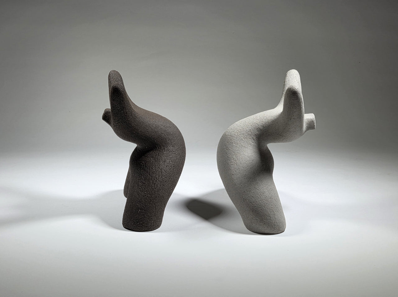 Black and grey abstract ceramic sculptures of two figures bent backwards with arms thrown outwards titled rock star on a light grey background