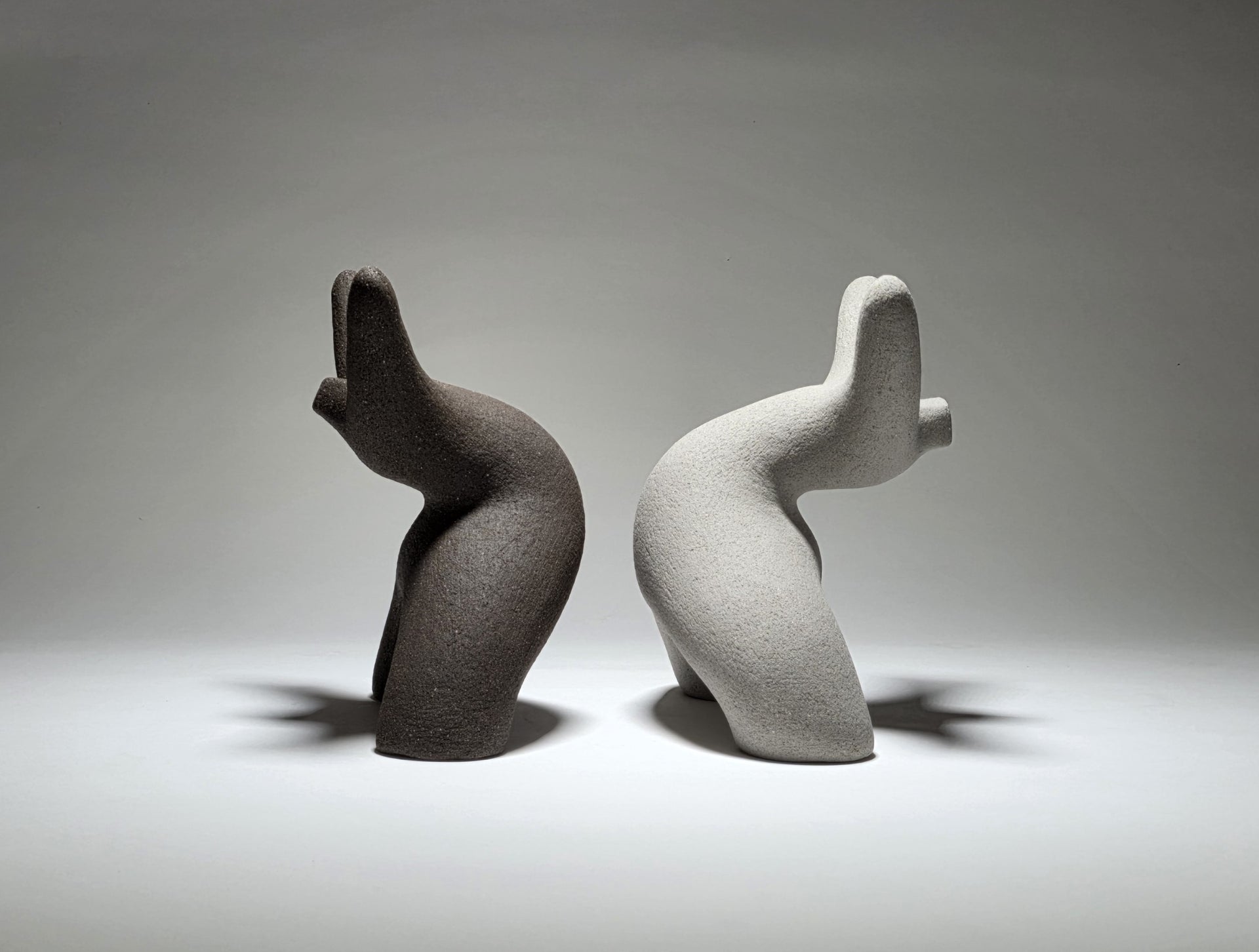 Black and grey abstract ceramic sculptures of two figures bent backwards with arms thrown outwards titled rock star on a light grey background