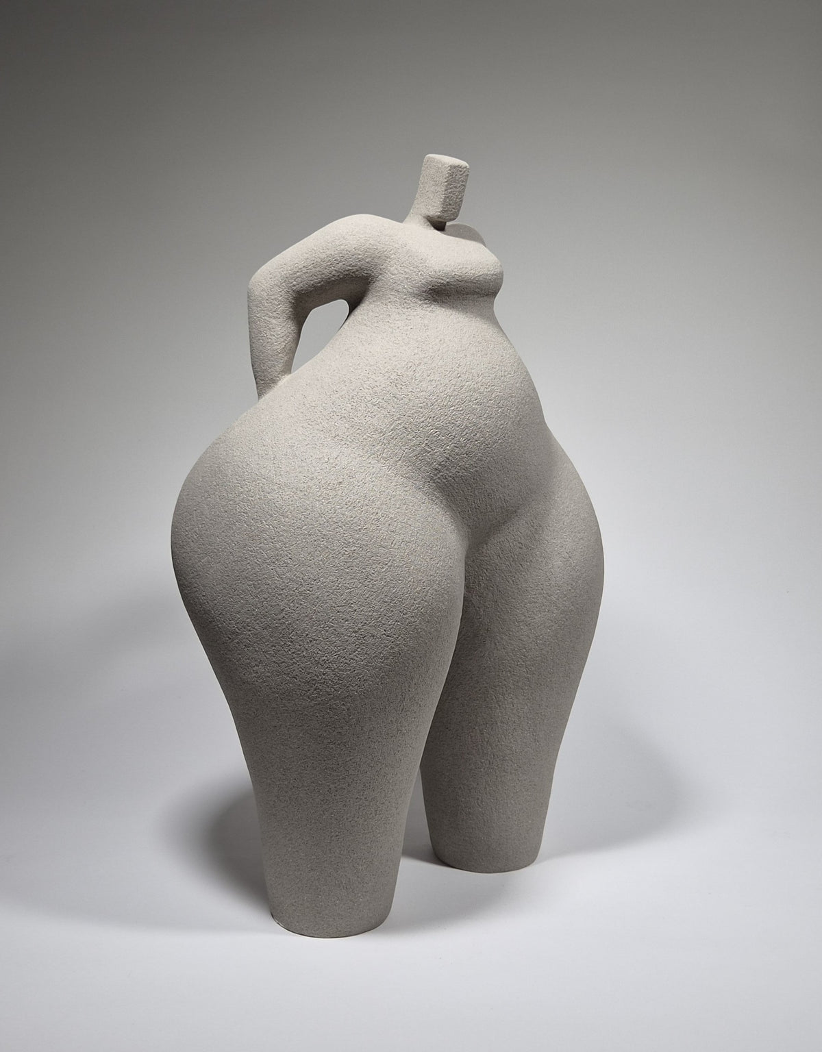 Still Standing, a hand-built ceramic sculpture of an abstracted female form in grey stoneware clay, grogged texture against a light grey background.