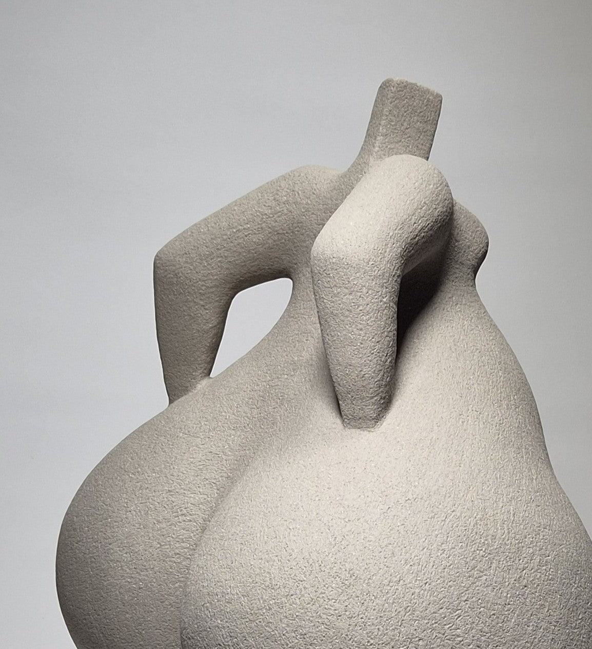 Close up of back of Still Standing, a hand-built ceramic sculpture of an abstracted female form in grey stoneware clay, grogged texture against a light grey background.