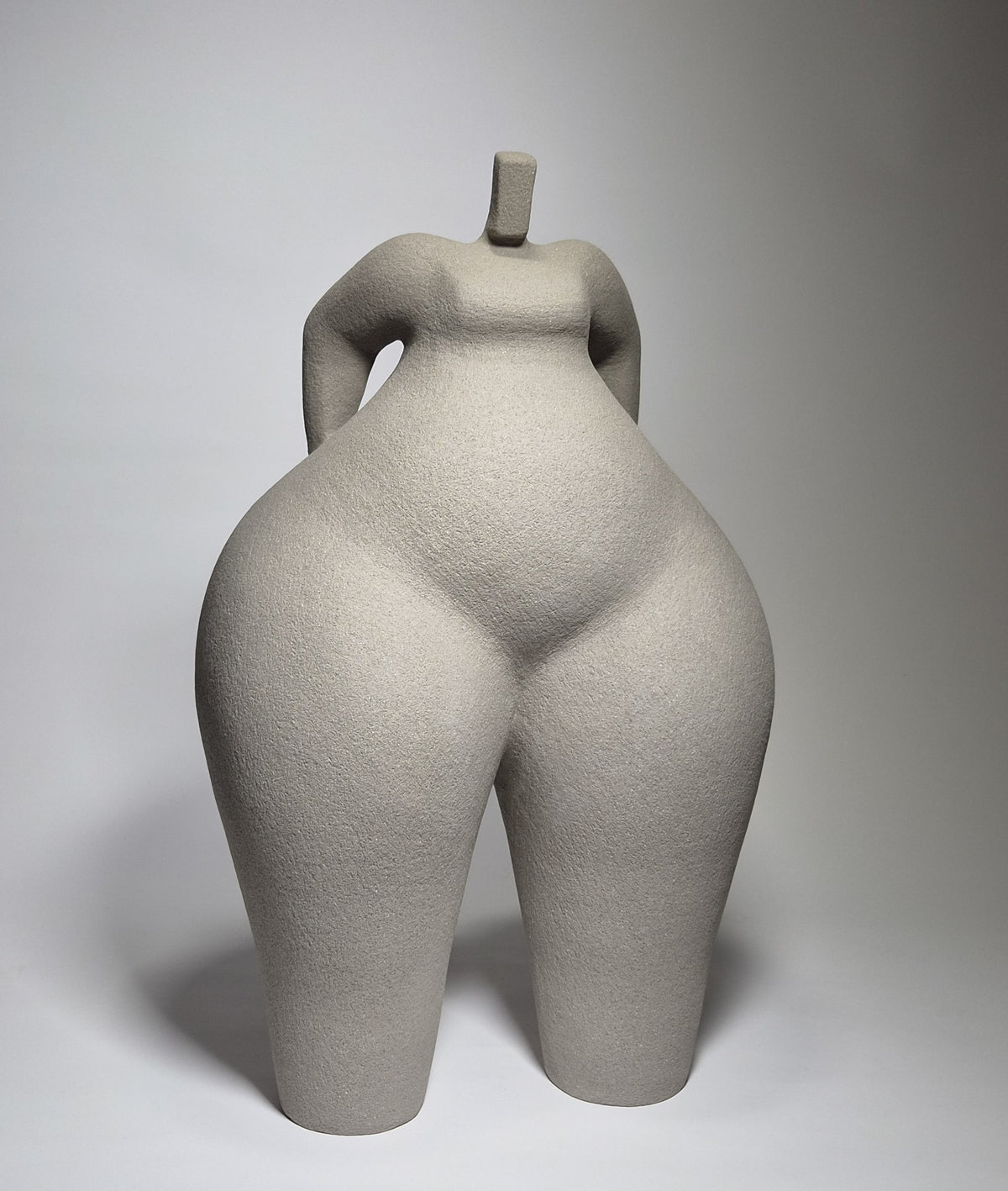 Still Standing, a hand-built ceramic sculpture of an abstracted female form in grey stoneware clay, grogged texture against a light grey background.