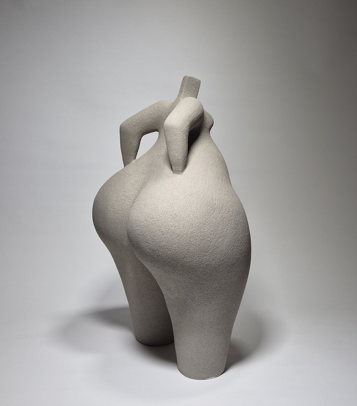 Rear shot of Still Standing, a hand-built ceramic sculpture of an abstracted female form in grey stoneware clay, grogged texture against a light grey background.