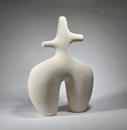 An abstract figurative ceramic sculpture with rounded legs and a branching upper torso, in a matte off-white finish on a light grey studio background.