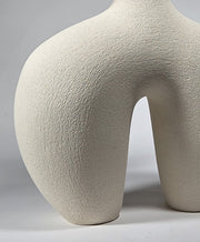 Close up of the bottom section of an abstract figurative ceramic sculpture showing rounded legs, in a matte off-white finish on a light grey studio background.