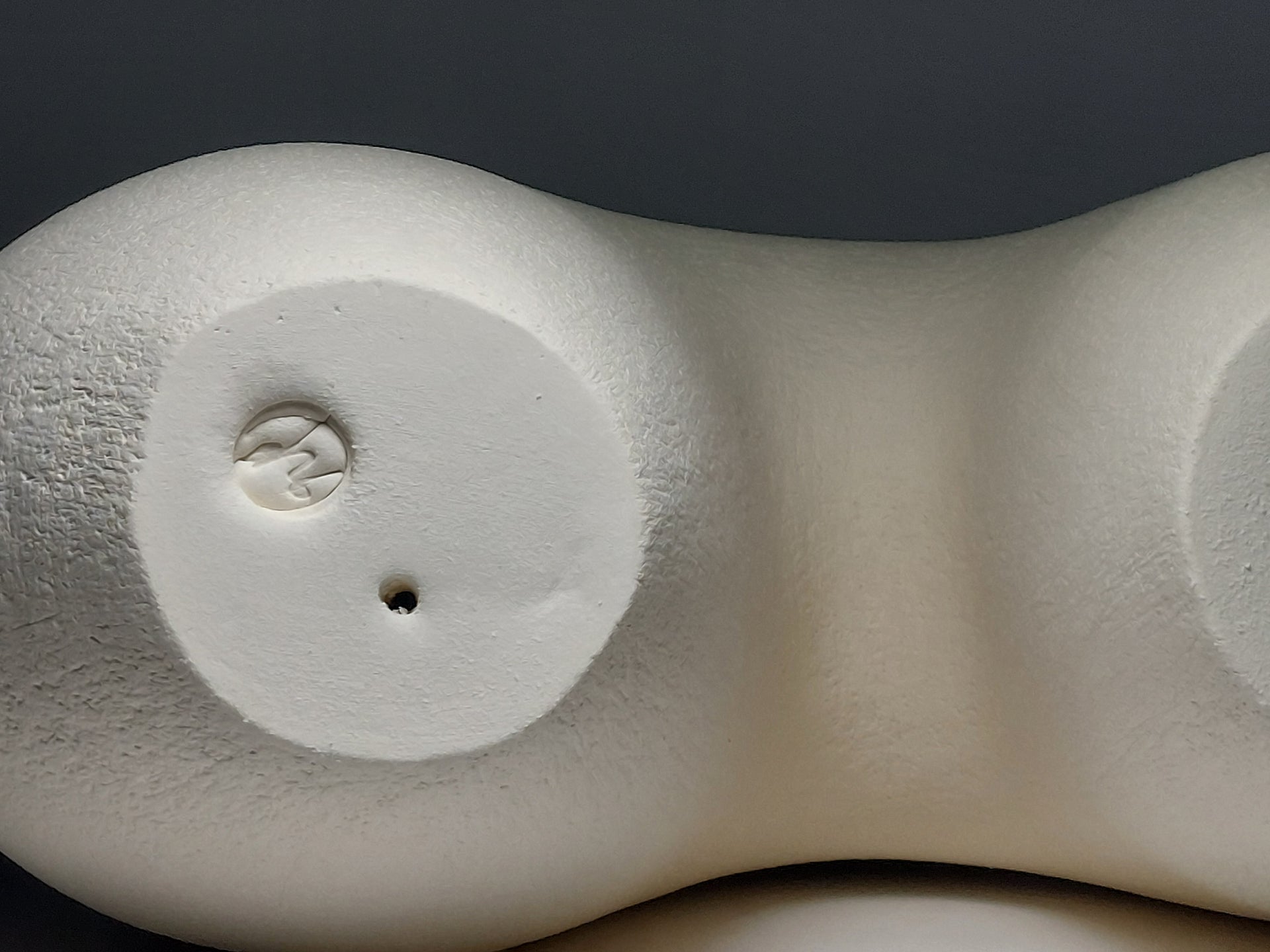 Base of An abstract figurative ceramic sculpture with rounded legs and a branching upper torso, in a matte off-white finish on a light grey studio background.