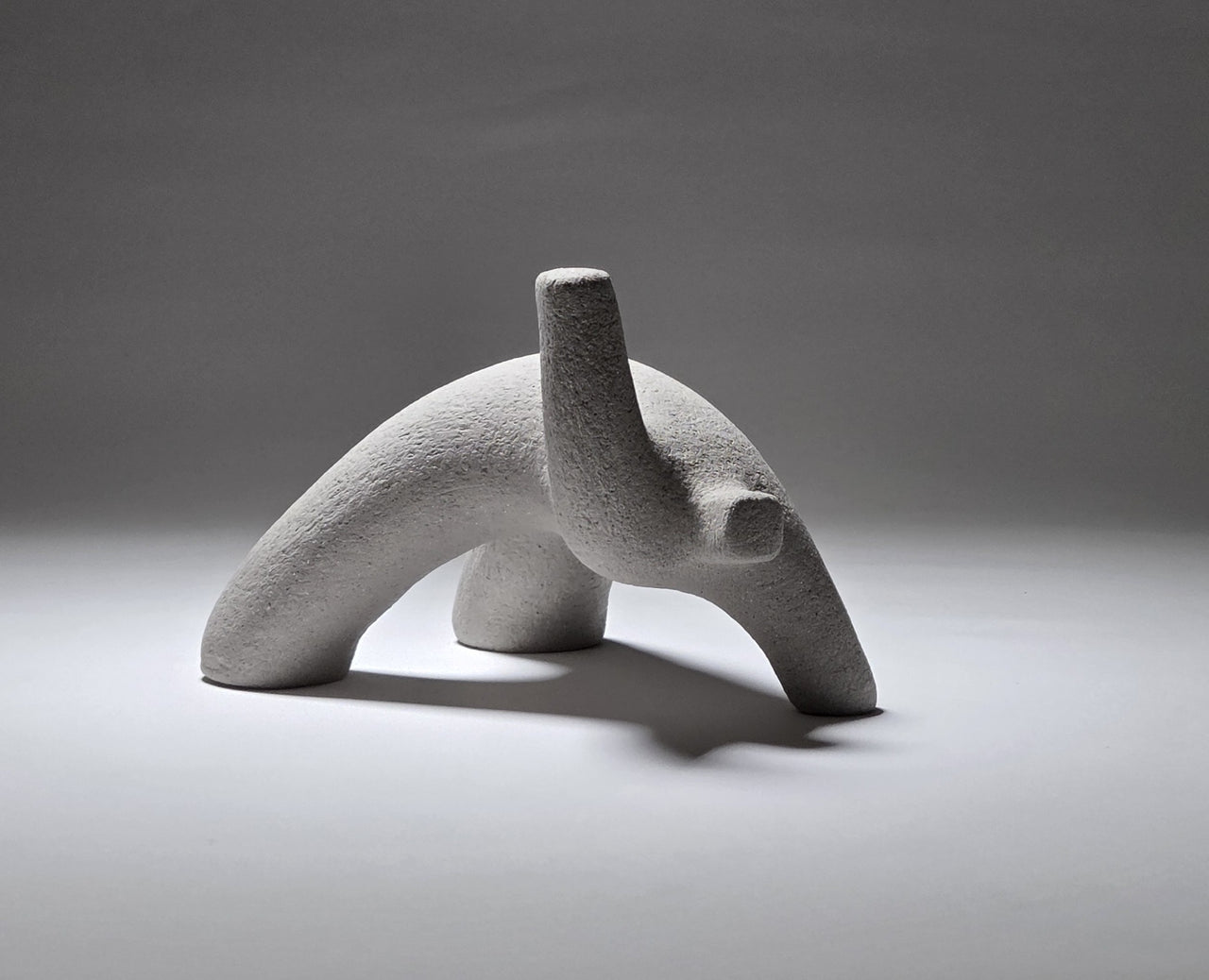 Abstract grey ceramic figure arching backwards with one arm on the floor and one stretched upwards pictures on a light grey background