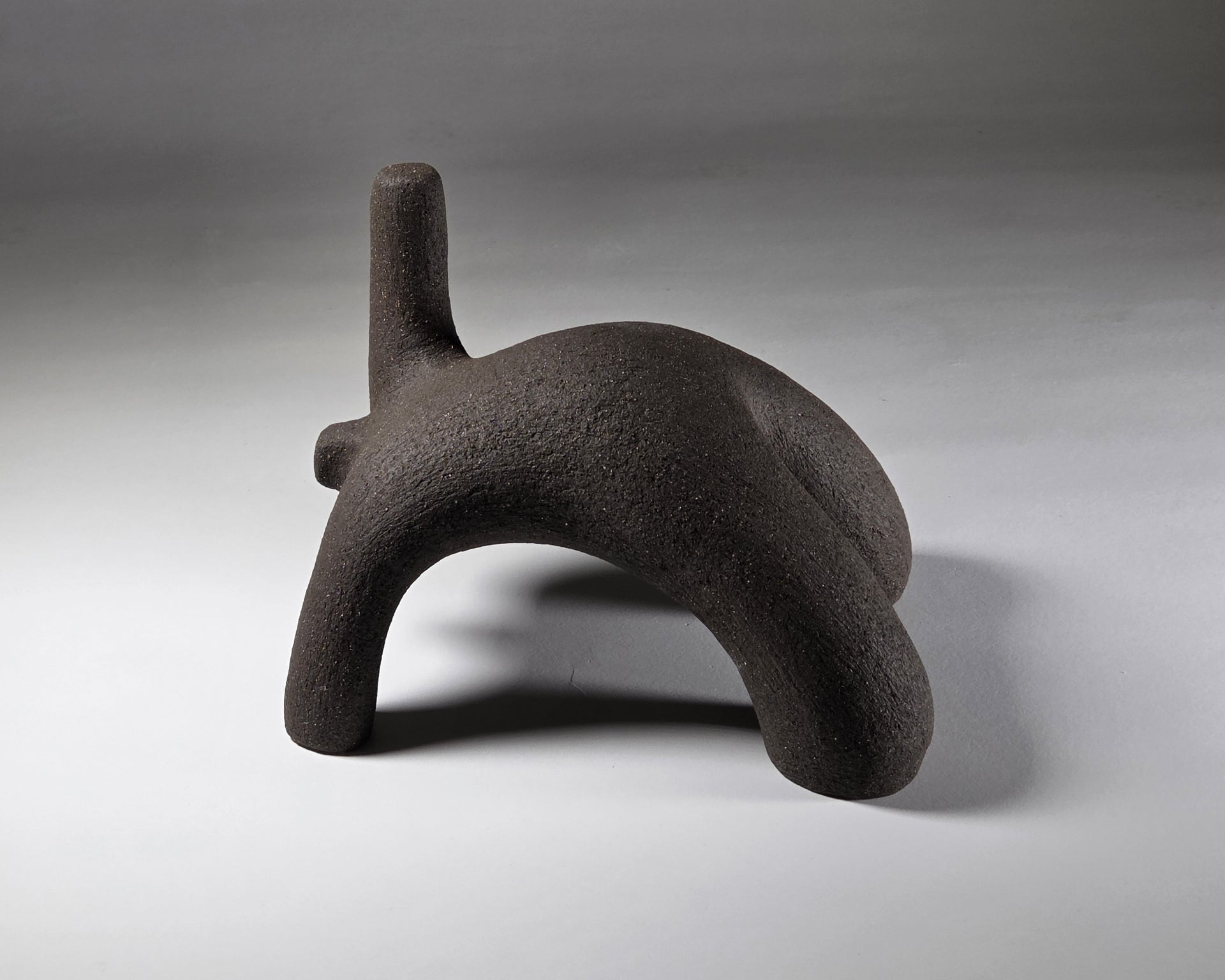 Abstract black ceramic figure arching backwards with one arm on the floor and one stretched upwards pictures on a light grey background