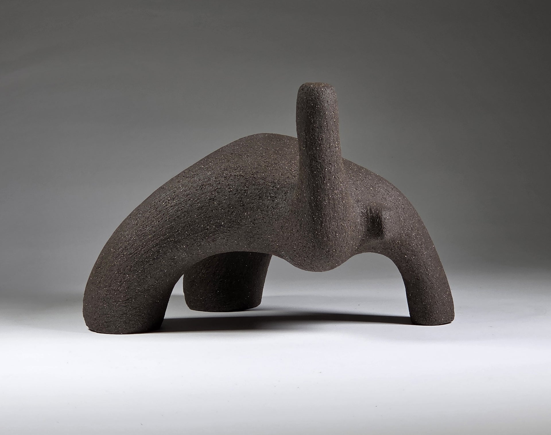 Abstract black ceramic figure arching backwards with one arm on the floor and one stretched upwards pictures on a light grey background