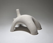 Abstract white ceramic figure arching backwards with one arm on the floor and one stretched upwards pictures on a light grey background