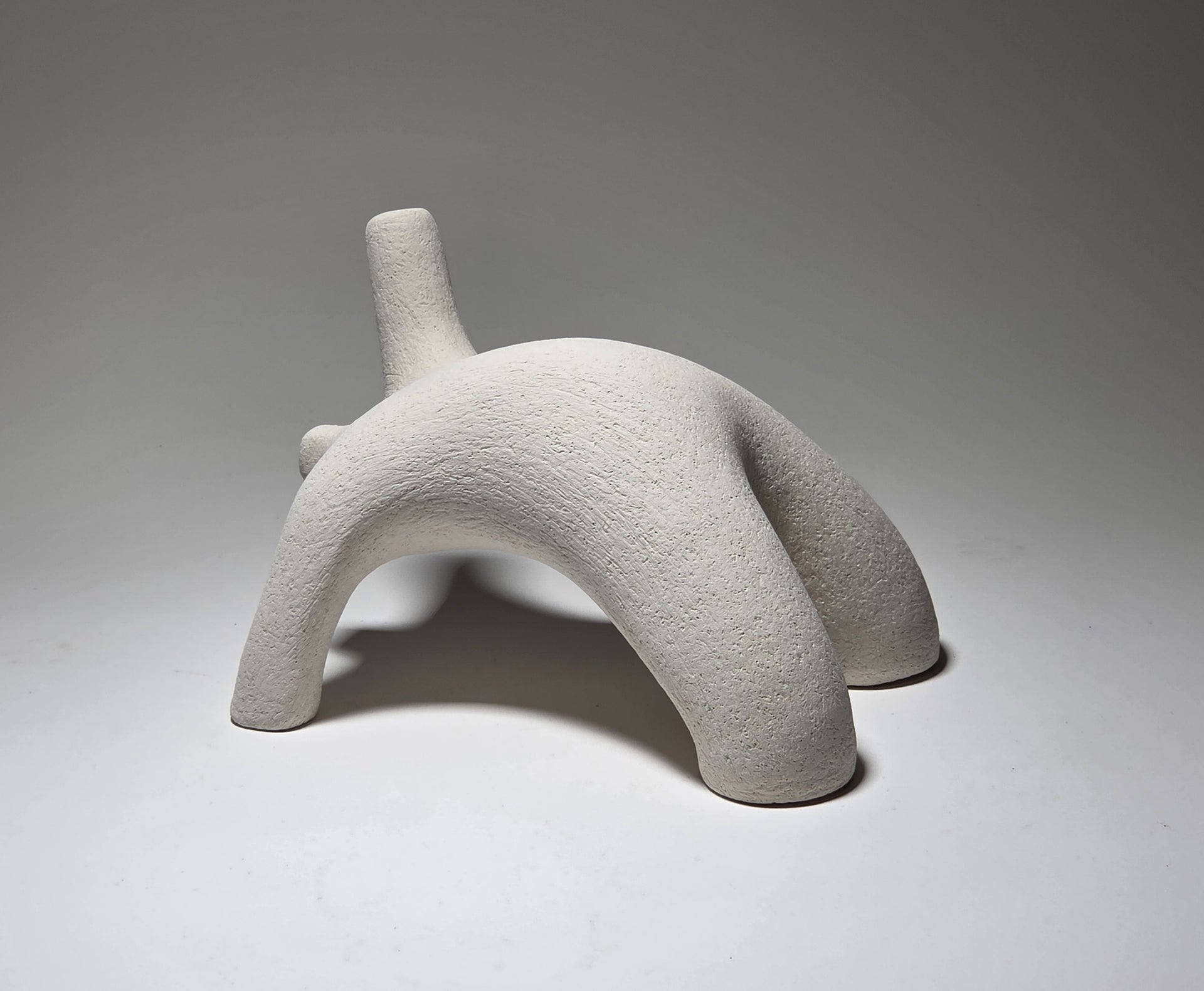 Abstract white ceramic figure arching backwards with one arm on the floor and one stretched upwards pictures on a light grey background