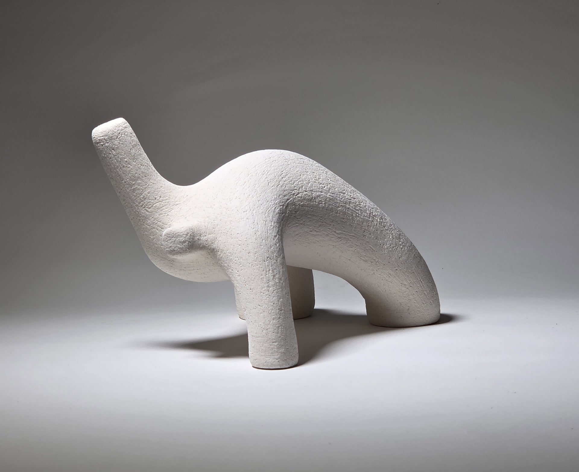 Abstract white ceramic figure arching backwards with one arm on the floor and one stretched upwards pictures on a light grey background