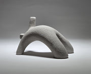 Abstract grey ceramic figure arching backwards with one arm on the floor and one stretched upwards pictures on a light grey background