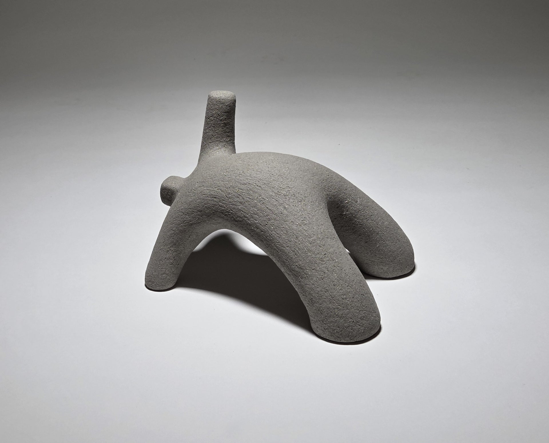 Abstract grey ceramic figure arching backwards with one arm on the floor and one stretched upwards pictures on a light grey background